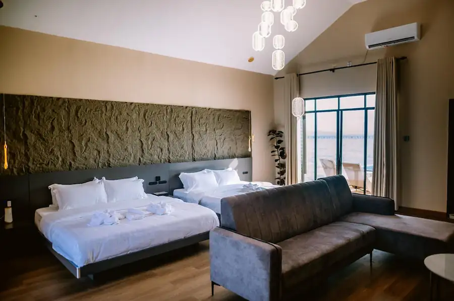 Spacious and modern interior of the Bedroom Deluxe Two Queen Beds at Turtle Seaweed Resort, featuring two beds, a large sectional sofa, and balcony access.